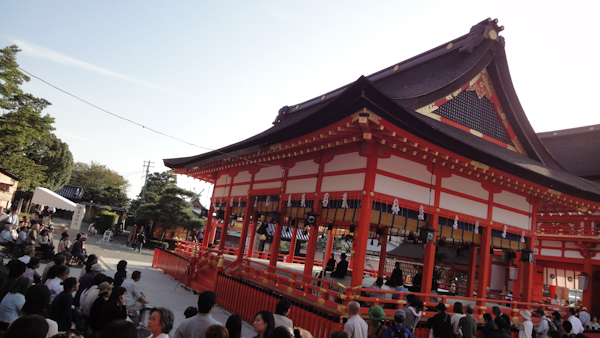 one of the main shrine buildings with the wall blinds open and people seated inside